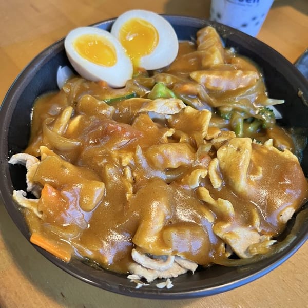 Madden Ramen's curry chicken with vegetables and two soft-boiled egg halves in a black bowl.