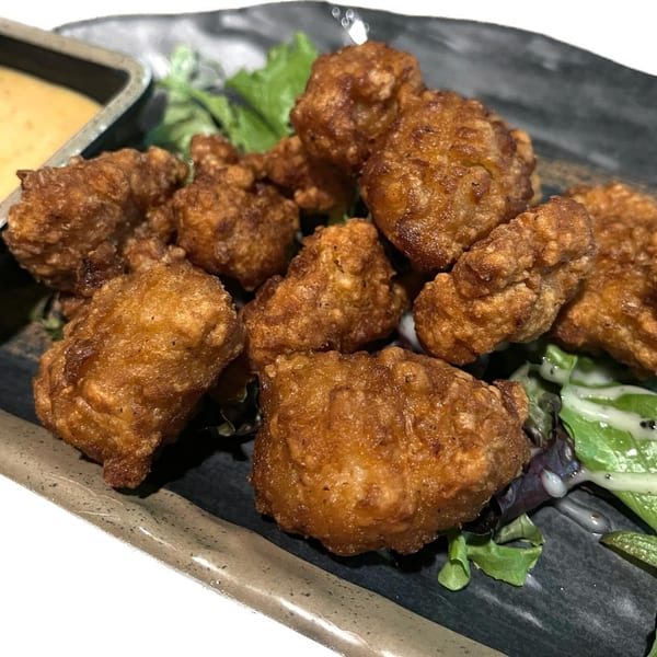 Crispy Madden Ramen karaage chicken pieces with a side of dipping sauce and greens.