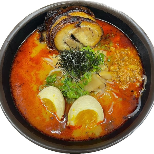 A bowl of Madden Ramen with a rich orange broth, pork belly, soft-boiled eggs, and green onions.