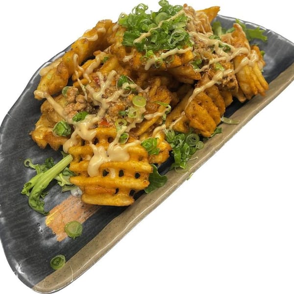 Madden Ramen's waffle fries topped with sauce, green onions, and seasoning on a dark plate.