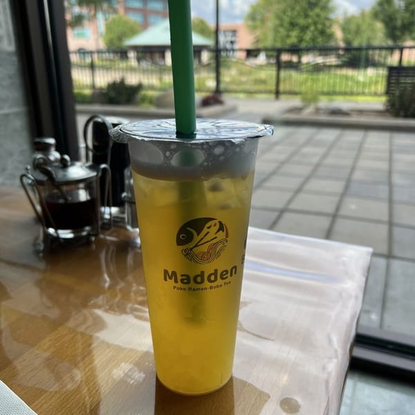 Madden Ramen's boba tea with a green straw on a wooden table, with an outdoor view.
