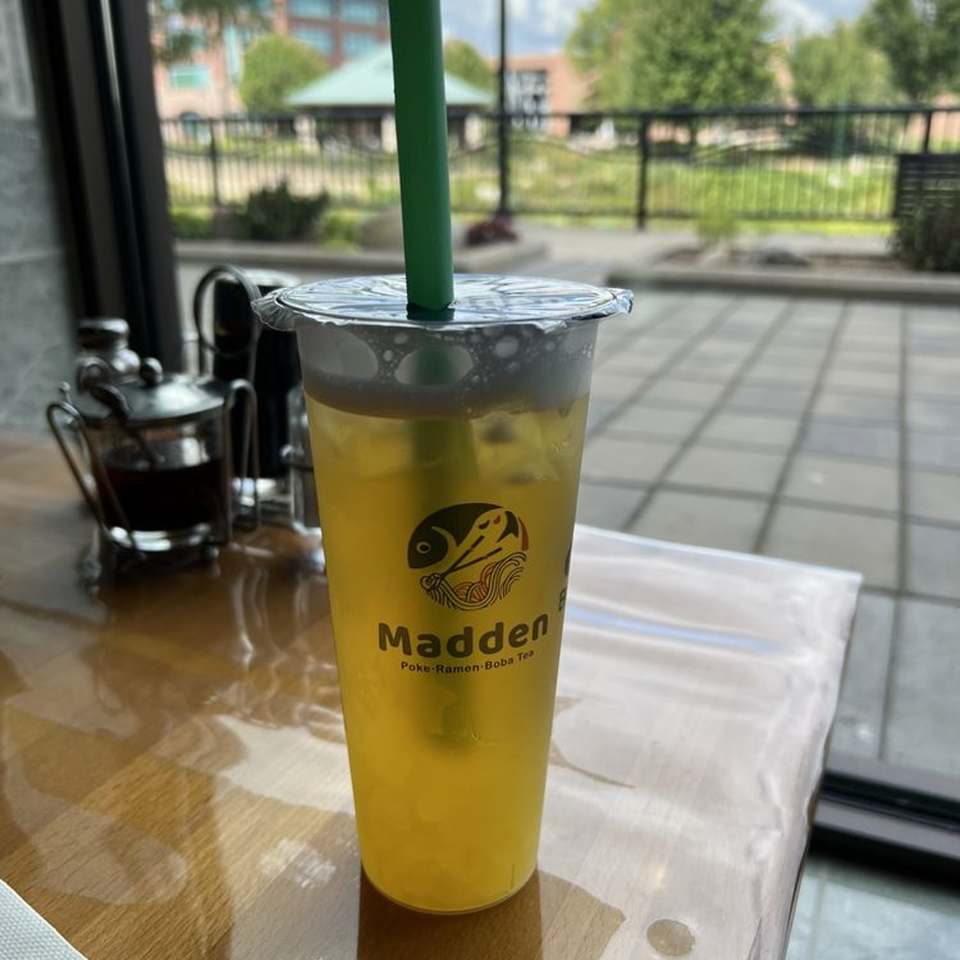 Madden Ramen's boba tea with a green straw on a wooden table, with an outdoor view.